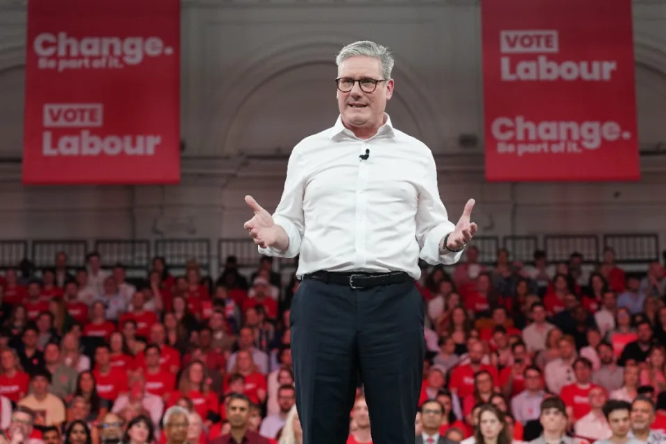 A white man in a white shirt, sleeves rolled up, wearing glasses and clip mic, gesturing with hands.