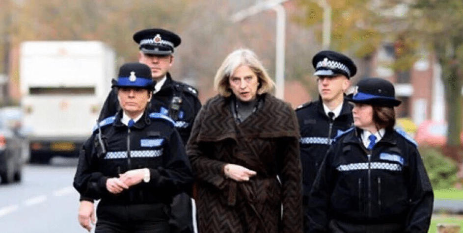 Theresa May walking with a police escort.